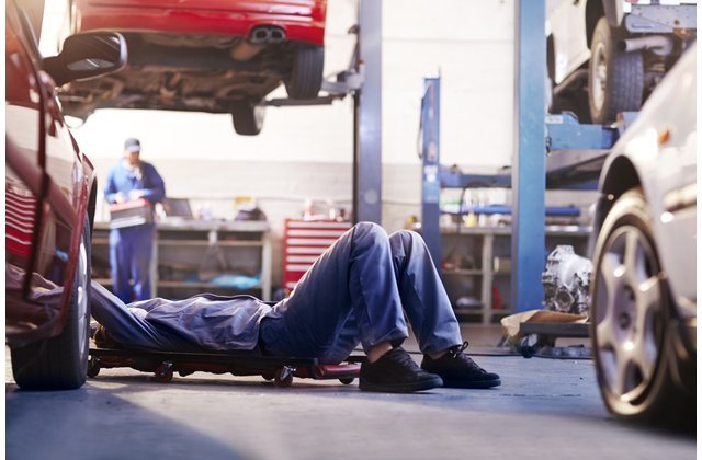 Auto technician in coveralls performing a visual inspection underneath a vehicle